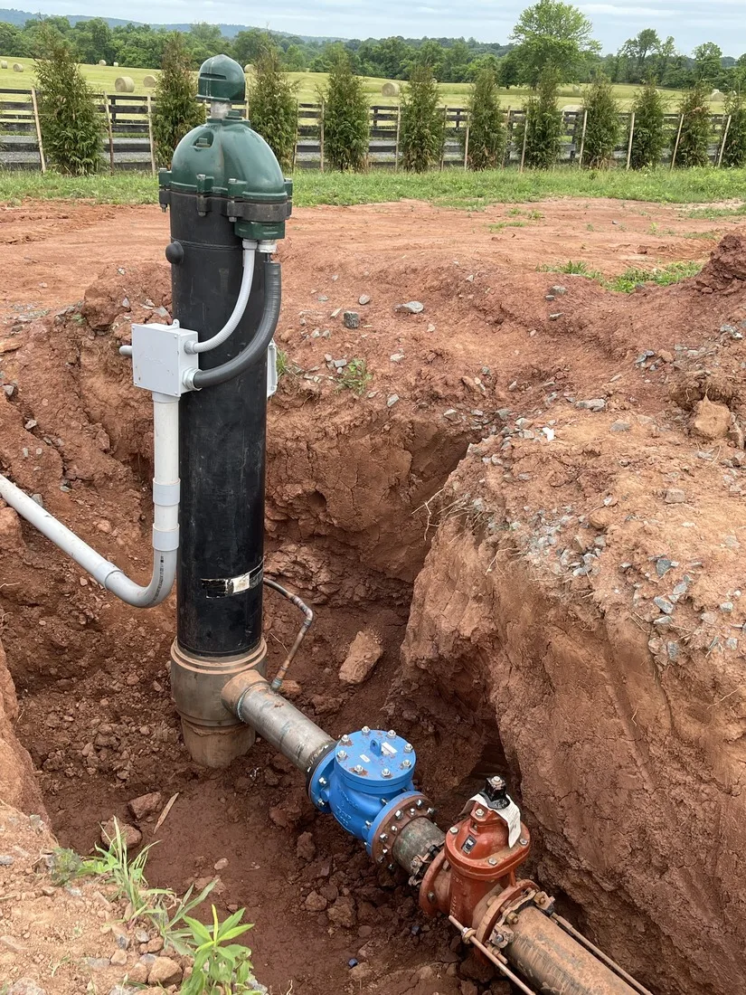 Finished well head with a green well cap, electrical junction box and water line valves in an open trench on a Maryland property
